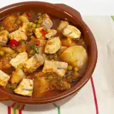 Un apetitoso marmitako de salmón, con trozos de pescado, patatas, guisantes y pimientos rojos, servido en cazuela de barro.