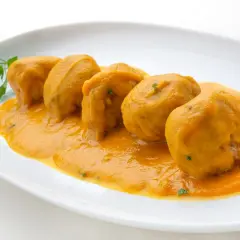 Cinco albóndigas en salsa arguiñano, servidas en un plato blanco con perejil fresco.