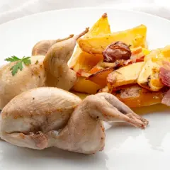 Dos codornices al horno, doradas y jugosas, acompañadas de patatas rústicas asadas con tocino y hierbas.