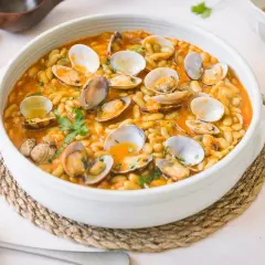 Plato de verdinas con almejas en salsa, decorado con perejil fresco. Un festín marinero y vegetal.
