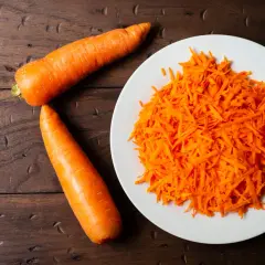 Dos zanahorias enteras y una porción de zanahoria rallada en un plato blanco. Preparando ingredientes para conocer el tiempo coccion zanahoria.