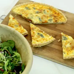 Un delicioso pastel de puerros recién horneado, cortado en porciones, junto a una ensalada fresca en un cuenco de madera.