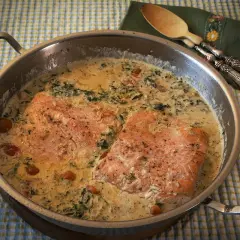 Dos filetes de salmón a la toscana en una sartén con salsa cremosa, espinacas y tomates cherry.