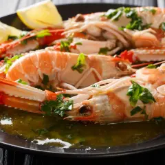 Cigalas a la plancha, jugosas y doradas, servidas con perejil picado y gajos de limón en un plato oscuro.