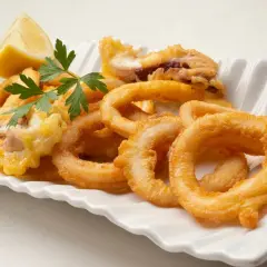 Calamares en salsa arguiñano, crujientes y dorados, servidos con limón y perejil en una fuente blanca.