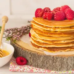 Una pila de tortitas de avena doradas, cubiertas con frambuesas frescas y miel, listas para disfrutar.
