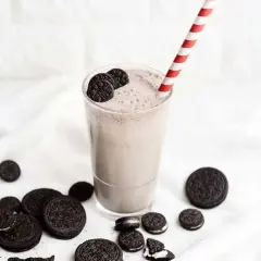 Delicioso batido de oreo cremoso, adornado con galletas enteras y trozos, listo para disfrutar con su pajita a rayas.