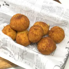 Croquetas de gambas doradas y crujientes, servidas sobre papel de periódico en una cesta metálica.