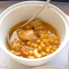 Un plato humeante de callos a la gallega, con garbanzos, chorizo y trozos de carne en una cazuela blanca.