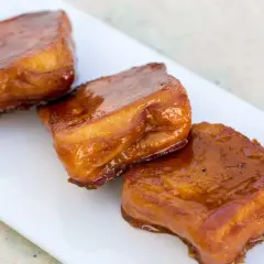 Tres torrijas de miel, doradas y brillantes, servidas en un plato blanco.