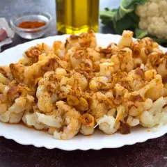 Coliflor al ajoarriero, con trozos dorados de ajo y pimentón, servida en un plato blanco.