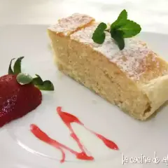 Un delicioso bizcocho de almendras espolvoreado con azúcar glas, decorado con una fresa y menta.