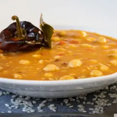 Un plato de garbanzos con arroz, reconfortante y sabroso, coronado con un pimiento seco y una hoja de laurel.