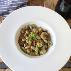 Plato de habas tiernas con jamón, ideal para tus recetas de habas. Servido en un cuenco blanco con menta fresca.