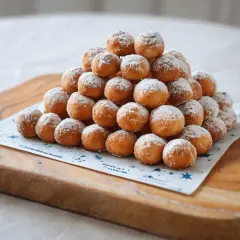 Montón de buñuelos de viento espolvoreados con azúcar glas sobre una tabla de madera.