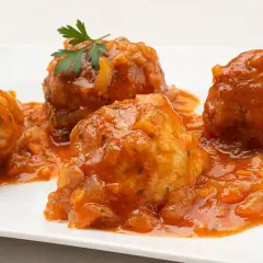 Cuatro albóndigas de rape en una salsa de tomate casera, decoradas con perejil fresco.