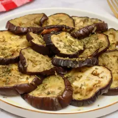 Rodajas de berenjenas al horno, doradas y espolvoreadas con hierbas aromáticas, listas para disfrutar.