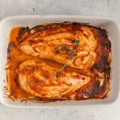 Dos jugosos solomillos de pavo al horno, dorados y con hierbas, reposan en una fuente blanca con asas turquesa.