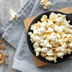 Palomitas recién hechas en sartén, listas para disfrutar. Maíz de palomitas en un cuenco y cuchara de madera.