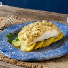 Delicioso bacalao a la portuguesa, servido sobre patatas y cubierto con cebolla caramelizada.