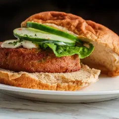 Deliciosa hamburguesa de salmón con lechuga, pepino y salsa cremosa en un pan tostado.