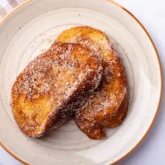Dos torrijas doradas y azucaradas en un plato, listas para disfrutar. ¡Perfectas si las haces en Thermomix!