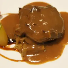 Carrilleras de ternera estofadas en salsa, acompañadas de patatas y un toque verde.
