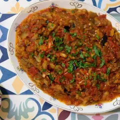Un plato de pisto con berenjena, lleno de verduras cocidas y espolvoreado con perejil fresco.