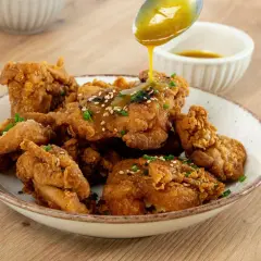 Crujiente pollo frito coreano bañado en salsa dorada, espolvoreado con semillas de sésamo y cebollín. ¡Un bocado irresistible!