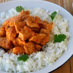 Sabroso pollo tikka masala servido sobre una cama de arroz blanco, decorado con hojas de cilantro fresco.