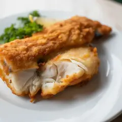 Un delicioso bacalao rebozado crujiente, con su interior blanco y tierno, servido con perejil y limón.