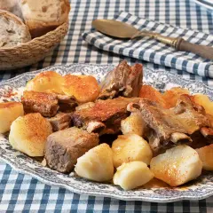 Un plato de carne o caldeiro con patatas cocidas y pan rústico en una cesta.