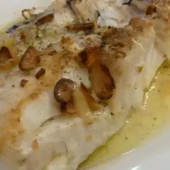 Merluza al horno sin patatas, jugosa y dorada, con láminas de ajo crujientes y hierbas aromáticas. Un plato ligero y sabroso.