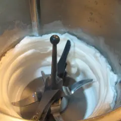 Montar claras a punto de nieve en Thermomix. La mezcla cremosa y blanca rodea las cuchillas.