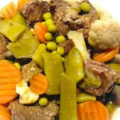 Ternera a la jardinera con trozos de carne tierna, zanahorias, guisantes, pimientos verdes y coliflor en un plato blanco.