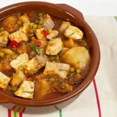 Un apetitoso marmitako de salmón, con trozos de pescado, patatas, guisantes y pimientos rojos, servido en cazuela de barro.
