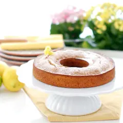 Bizcocho de limón Thermomix esponjoso y dorado, espolvoreado con azúcar glas. Limones y lima frescos al lado.