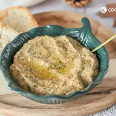 Delicioso pate de berenjena cremoso, servido en un cuenco verde con un toque de aceite de oliva y perejil. Acompañado de tostadas crujientes.