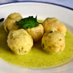 Cinco albóndigas de merluza caseras flotan en una salsa verde cremosa, adornadas con una ramita de perejil fresco.