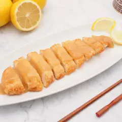 Pollo al limón chino servido en una bandeja blanca, con limones frescos y palillos de madera.