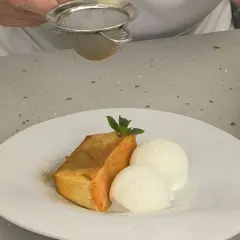 Un trozo de flan de calabaza Arguiñano, espolvoreado con canela, acompañado de dos bolas de helado de vainilla y una hoja de menta.