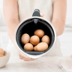 Manos sostienen el recipiente de la Thermomix lleno de huevos, listos para cocer huevos thermomix.
