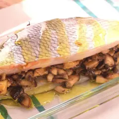 Pescado relleno de setas al horno, jugoso y dorado, listo para servir en una fuente de cristal.