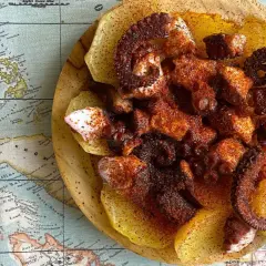 Pulpo con patatas, un plato gallego servido sobre un mapa antiguo. Tentáculos de pulpo especiados y tiernos sobre rodajas de patata.