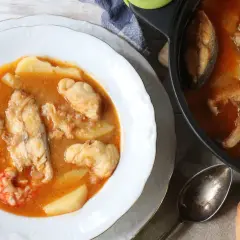 Un delicioso suquet de pescado con patatas y gambas, servido en un plato blanco y una cazuela.