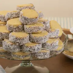 Montón de alfajores de maicena cubiertos de coco rallado, apilados en una fuente de vidrio.