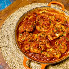 Pollo en salsa roja, como las recetas de pollo en salsa de la abuela, servido en cazuela naranja sobre esterilla de mimbre.