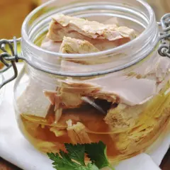 Un frasco de vidrio con atún en escabeche, listo para disfrutar. Unas hojas de perejil adornan la escena.