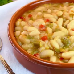 Judías blancas de bote salteadas con pimientos y cebolla, servidas en cuenco de barro.