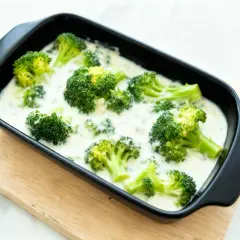 Brocoli con bechamel cremoso en una bandeja negra, listo para hornear. Un plato reconfortante y delicioso.